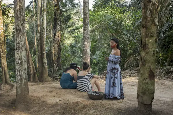 Due donne si siedono sul pavimento della foresta pluviale, un'altra donna si alza e guarda di lato in un abito lungo