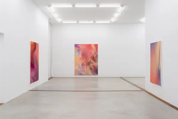 Kuva valkoisesta kuutiohuoneesta vaaleanpunaisilla abstrakteilla maalauksilla.