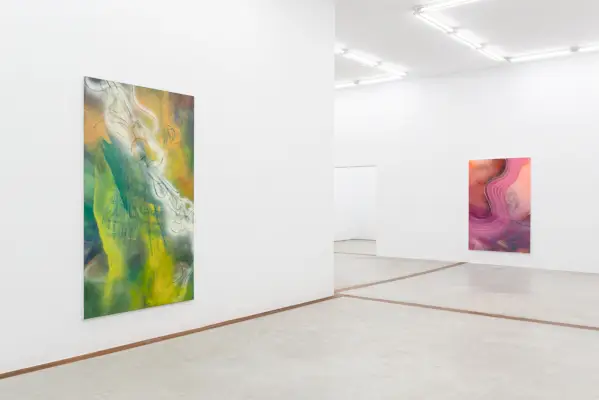 Huoneessa on abstrakteja maalauksia keltaisen ja vihreän sävyillä.