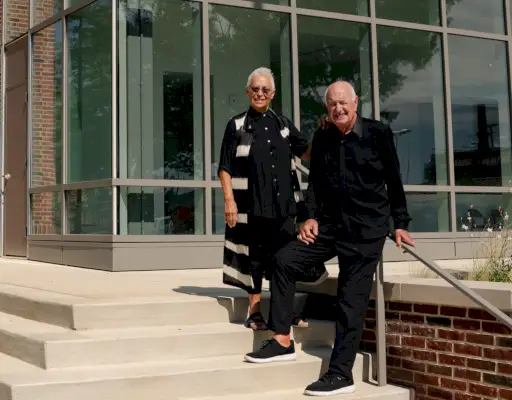 Un uomo e una donna vestiti di nero posano all'esterno dell'edificio sui gradini