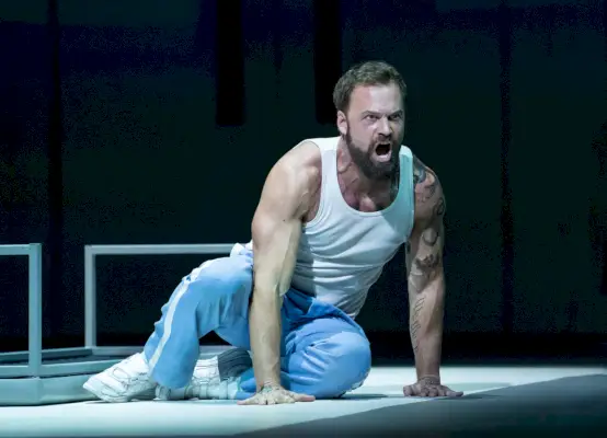 Mies farkuissa ja toppiin istuu lavalla ja laulaa vihaisesti