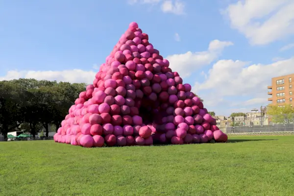 Duża piramida zbudowana z czegoś, co przypomina fioletowe balony stojące na trawiastym polu