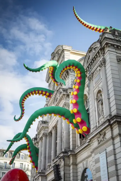 Z okien dużego kamiennego budynku roją się duże, zielone i żółte macki ośmiornicy