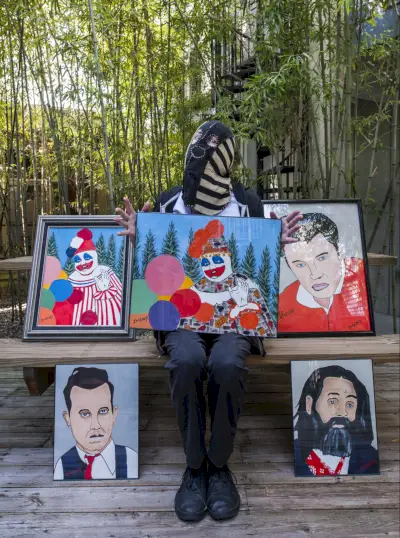 Ryan Graveface (maskeret) poserer med nogle af sine yndlings Gacy-malerier,