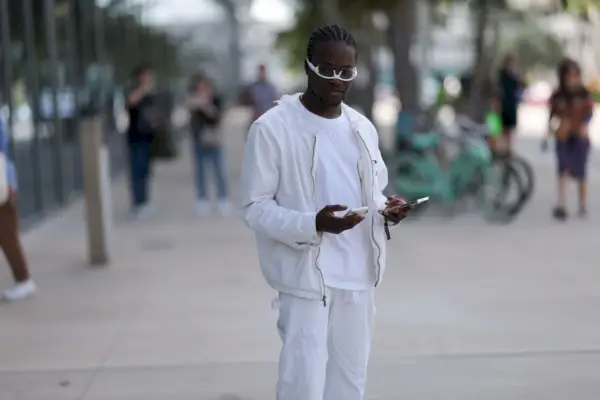 Un uomo con la pelle scura in un abito completamente bianco indossa occhiali da sole capovolti in una strada trafficata