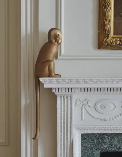 Mała rzeźba małpy z brązu stoi na białym kominku.