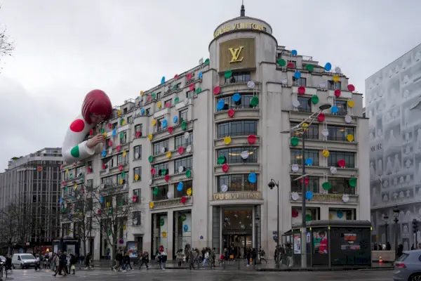 Duży wielopiętrowy budynek zajmujący bryłę ma rzeźbę kobiety umieszczającej kolorowe kropki na budynku zwisającym z dachu