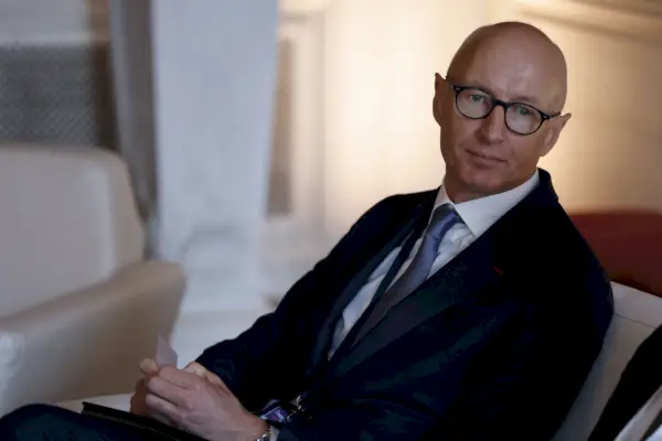 Kalju mies, jolla on silmälasit mustassa puvussa, nojautuu tuoliin