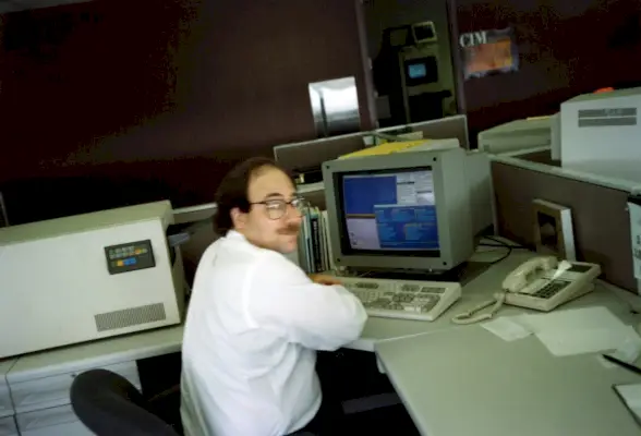 Foto sfocata di un uomo con gli occhiali seduto al cubicolo davanti al computer