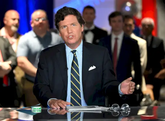 Tucker Carlson puhuu uutispöydässä toinen käsi koholla.