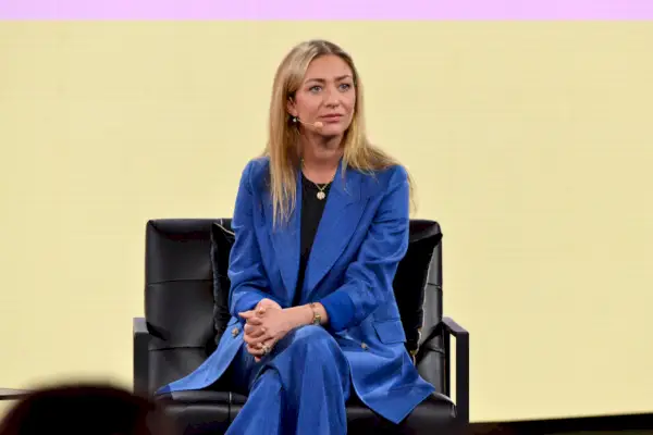 Whitney Wolfe Herd, CEO di Bumble, seduta su una sedia nera con indosso un abito blu