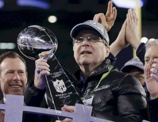 Paul Allen, medelålders vit kille med basebollhatt, håller Superbowl-trofén