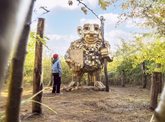 Un bambino guarda una gigantesca statua di legno di un troll