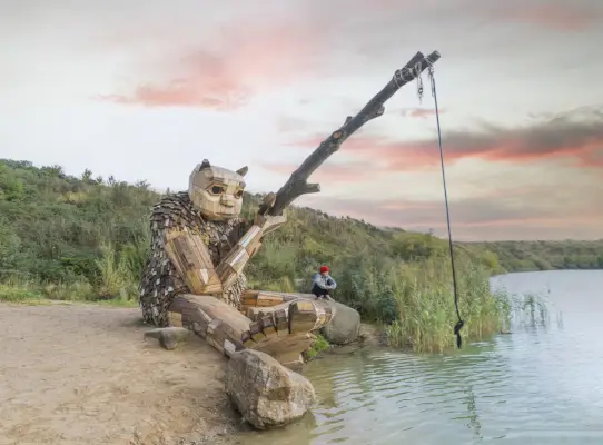 Una gigantesca statua di legno di un troll pesca in uno stagno