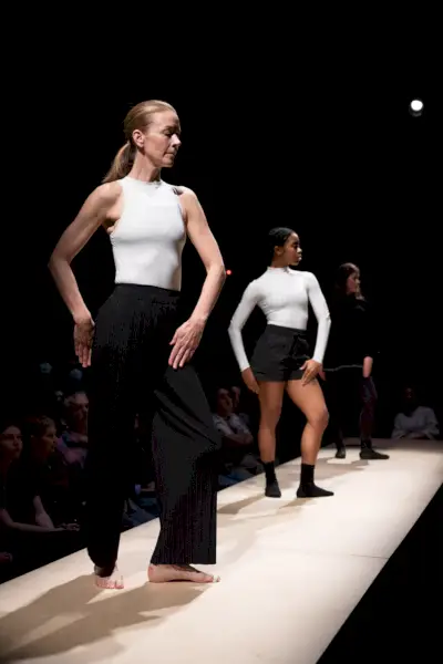 Duas dançarinas com blusas brancas e calças pretas estão em uma mesa branca