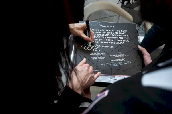 Una persona con i capelli lunghi firma il retro della copertina di un disco in vinile nero con un pennarello argentato.