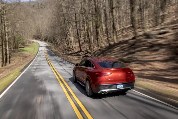 tył czerwonego mercedesa jadącego drogą otoczoną drzewami.