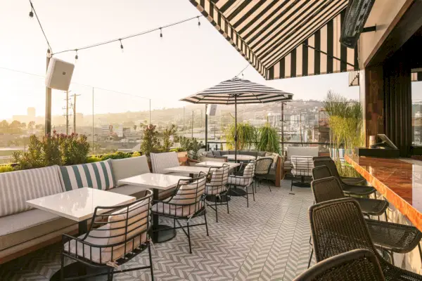 Un ristorante sul tetto con pavimenti in chevron bianchi, tavoli bianchi e sedie e tende da sole a strisce bianche e nere.