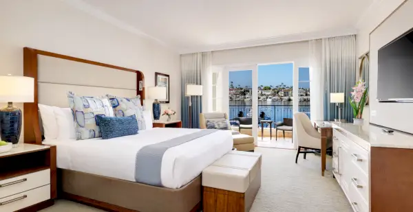 Gästrum med en säng till vänster, TV till höger och vattenutsikt i bakgrunden med balkong.