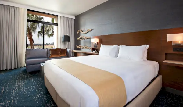 Gästrum på Hyatt Regency John Wayne Airport Newport Beach med en säng och fönster från golv till tak i bakgrunden.