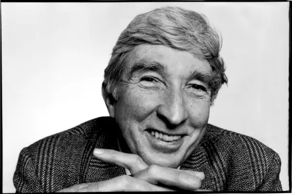 Czarno-biały portret mężczyzny w średnim wieku, patrzącego bezpośrednio w kamerę, z brodą opartą na dłoniach.