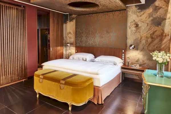 Apartament Ludwiga z łóżkiem pośrodku z malowidłami ściennymi za nim i żółtym aksamitnym kufrem z przodu.