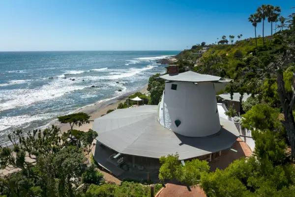 Pyöreä rantakoti vihreiden puiden ja sinisen merinäköalan ympäröimänä.