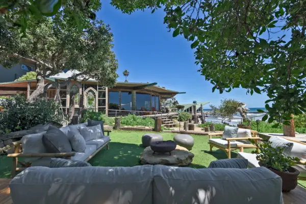 Eloisa vihreä nurmikko leveiden puiden varjossa. Nurmikon huonekalut avautuvat laajalle merinäköalalle.