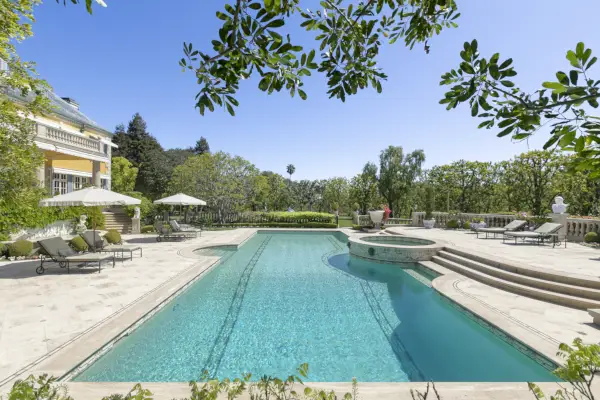 Una lunga piscina al centro di una terrazza in pietra bianca immersa nel verde.