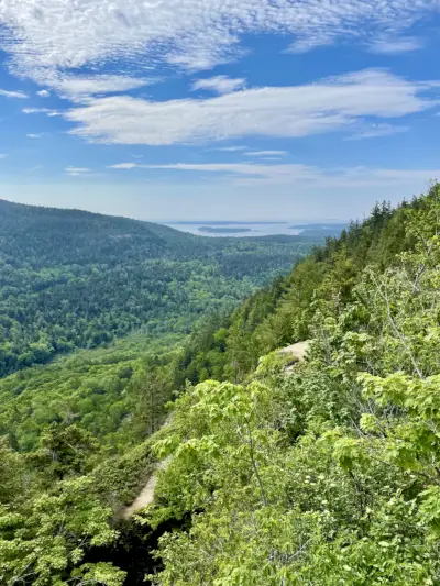 Rehevän vihreät vuorenrinteet, vesi horisontissa, sininen taivas ja pilvet yläpuolella.