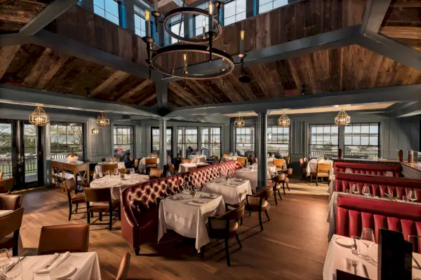 L'interno di un ristorante elegante con separé rossi, tovaglie bianche e pavimenti e soffitti in legno marrone con molte finestre