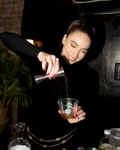 En kvinna med en hästsvans ler när hon häller upp en drink.