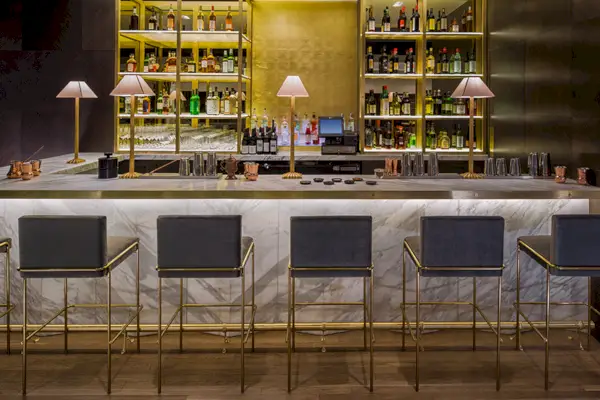 En inomhusbar i marmor med guldbakgrund, svarta stolar och trägolv.