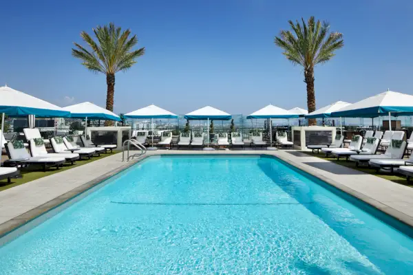 Basen na dachu otoczony białymi leżakami i białymi parasolami z turkusowymi wykończeniami.