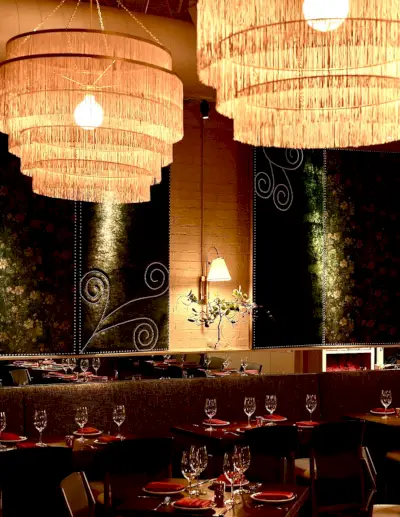 Tyylikkään ravintolan sisustus isoilla riippuvaloilla, ikkunoilla yksityiskohdilla, punaisilla kattauksilla ja himmeällä valaistuksella.