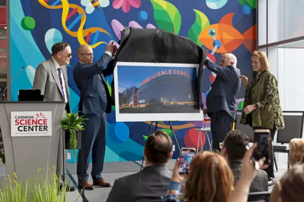 Neljä ihmistä seisoo korokkeella ja paljastaa valokuvan uudesta museosta