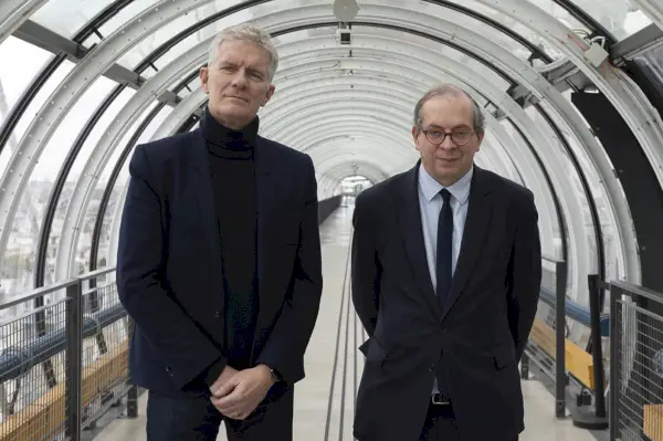 Kaksi miestä seisoo läpinäkyvässä putkessa