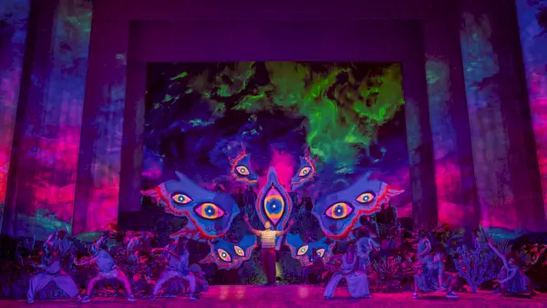 Mies seisoo lavalla aavemaisen värikkäiden silmien ympäröimänä