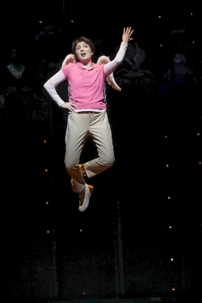 Wykonawca operowy w spodniach khaki, różowej koszuli i małych pierzastych skrzydełkach